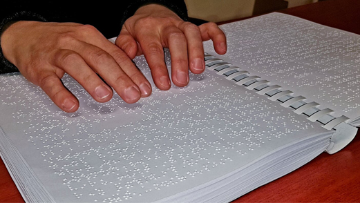 egy férfi éppen egy braille könyvet olvas az ujjai segítségével